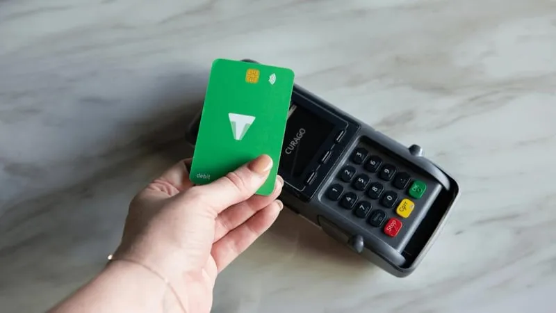 A hand holding a contactless card over a card payment terminal